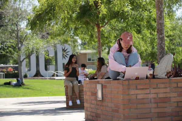 Student sitting on a brick ledge in front of her laptop, outside by the UCR statue